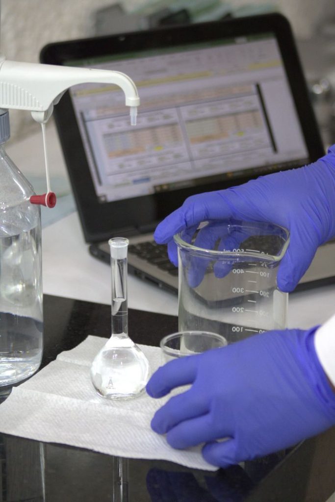 Scientist in gloves with beaker and laptop in a lab, conducting experiments.